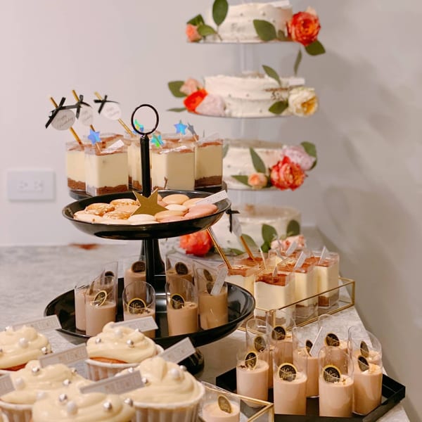 A dessert table with a tiered cake, cupcakes, macarons, and various parfaits from Studio Multisweet.