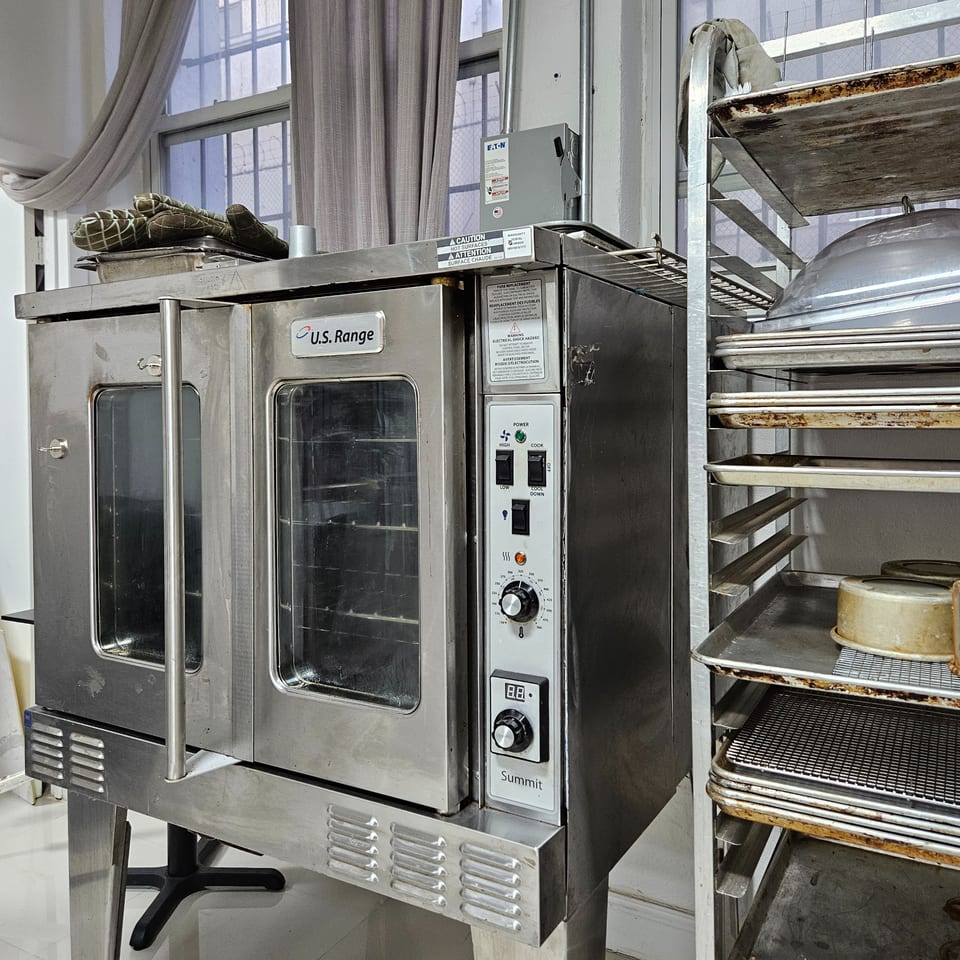 A stainless steel U.S. Range commercial oven and a metal rack with baking sheets in a dessert kitchen.