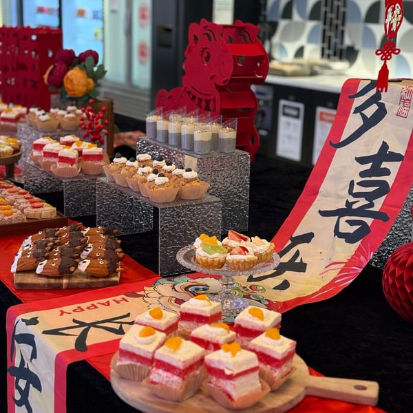 A buffet table with various desserts, including red and white layered cakes, tarts, and madeleines.