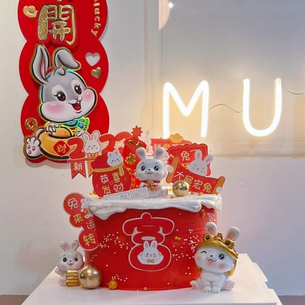 A red Studio Multisweet cake with rabbit figurines, gold accents, and Chinese New Year decorations.
