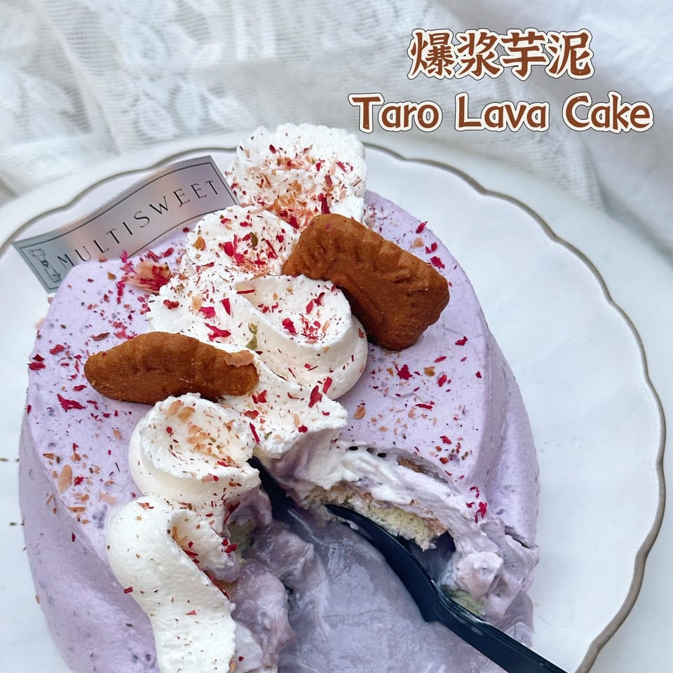 A Studio Multisweet Taro Lava Cake, purple with whipped cream, cookies, and red sprinkles, with a slice removed.