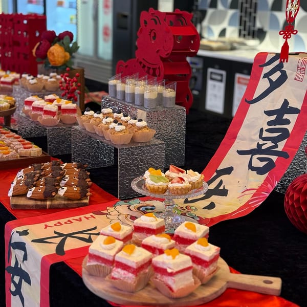 A dessert buffet with various pastries, tarts, and cupcakes, decorated with red Chinese New Year accents.