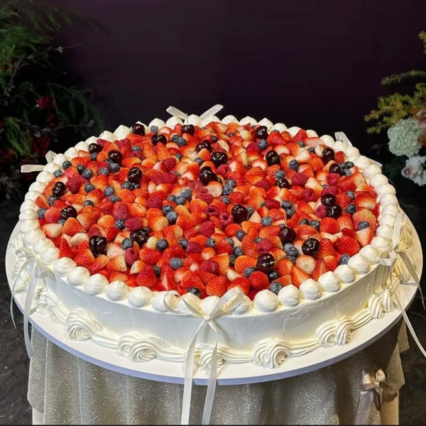 A large, round Studio Multisweet cake, generously topped with strawberries, blueberries, raspberries, and cherries.