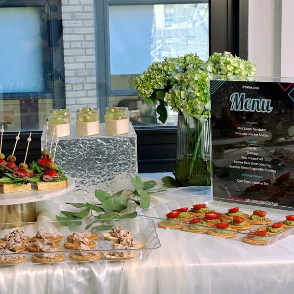 A Studio Multisweet dessert buffet with savory bites, desserts, and a menu on a white tablecloth.