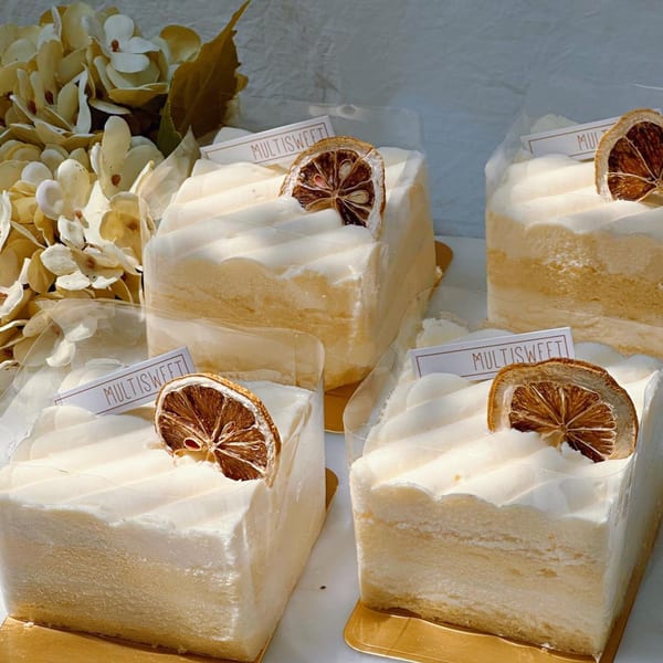 Four Studio Multisweet dessert cakes with white frosting, dried orange slices, and decorative flowers.