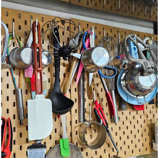 Baking tools and utensils, including whisks, spatulas, and measuring cups, hanging on a pegboard.