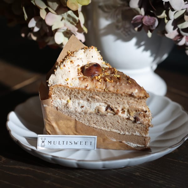 A slice of Studio Multisweet chestnut cake with cream and nuts on a white plate.