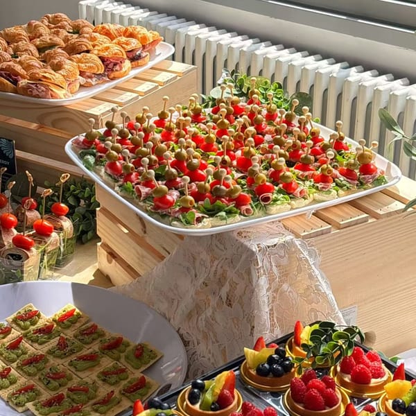 A buffet table with mini croissants, canapés, fruit tarts, and avocado crackers.
