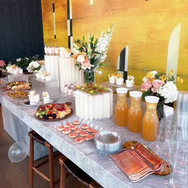 A Studio Multisweet dessert buffet with fruit platters, cupcakes, drinks, and floral arrangements.