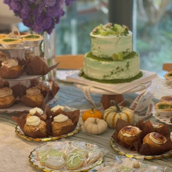 A Studio Multisweet dessert table with a two-tiered green cake, cupcakes, tarts, and cookies.