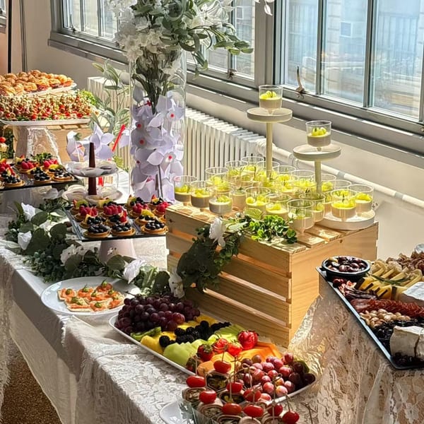 A dessert buffet with fruit tarts, mini parfaits, fruit platters, and savory appetizers on a white tablecloth.