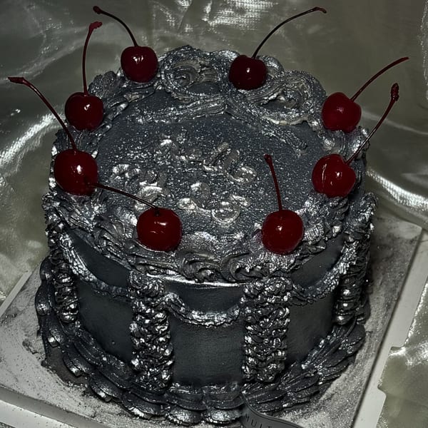 A Studio Multisweet dessert, a round silver cake with ornate frosting and eight red cherries on top.
