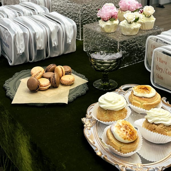 Studio Multisweet macarons, cream puffs, and floral cupcakes on a dark green tablecloth.