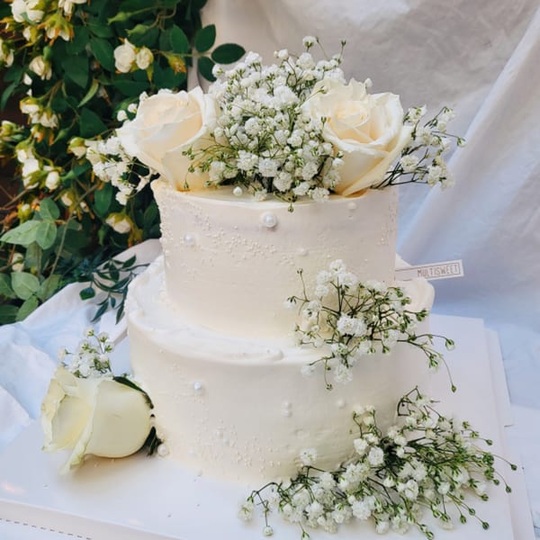 Two-tiered white cake from Studio Multisweet, adorned with white roses, baby's breath, and pearl accents.