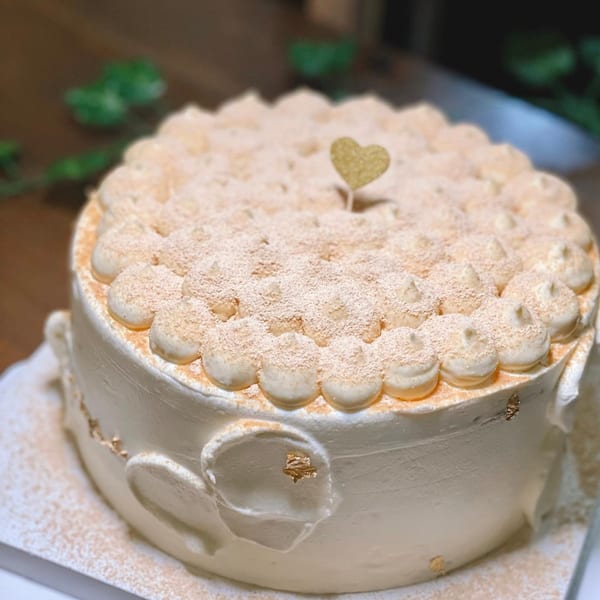 A Studio Multisweet dessert cake, topped with cream dollops, powdered sugar, and a golden heart.