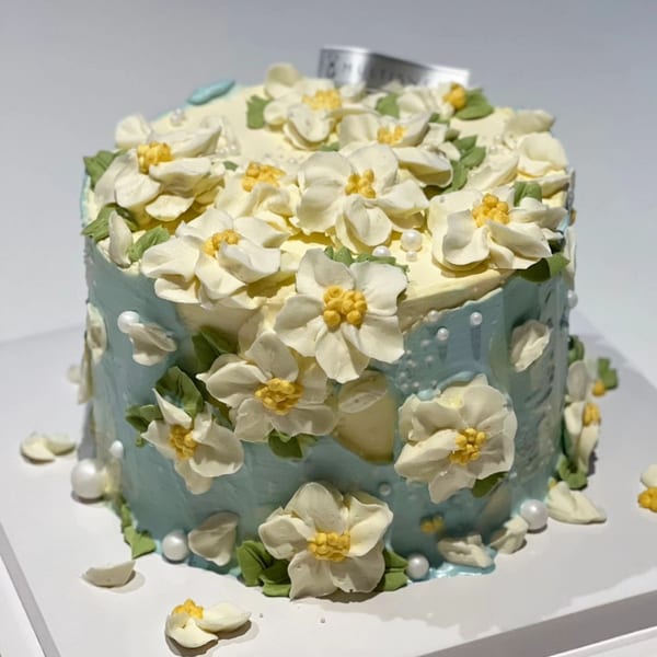 A Studio Multisweet dessert cake, light blue with white and yellow buttercream flowers and pearl accents.