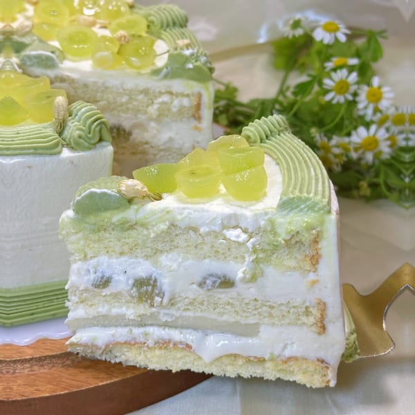 A slice of Studio Multisweet's green grape cake with cream and green frosting, next to a whole cake.