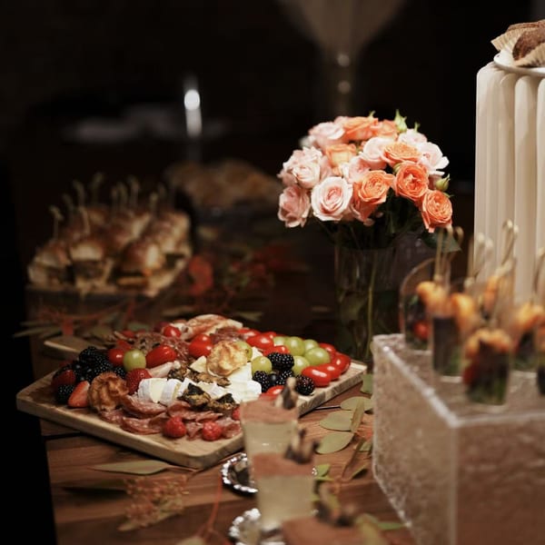 A charcuterie board with cheeses, meats, and berries, alongside flowers and other appetizers on a table.